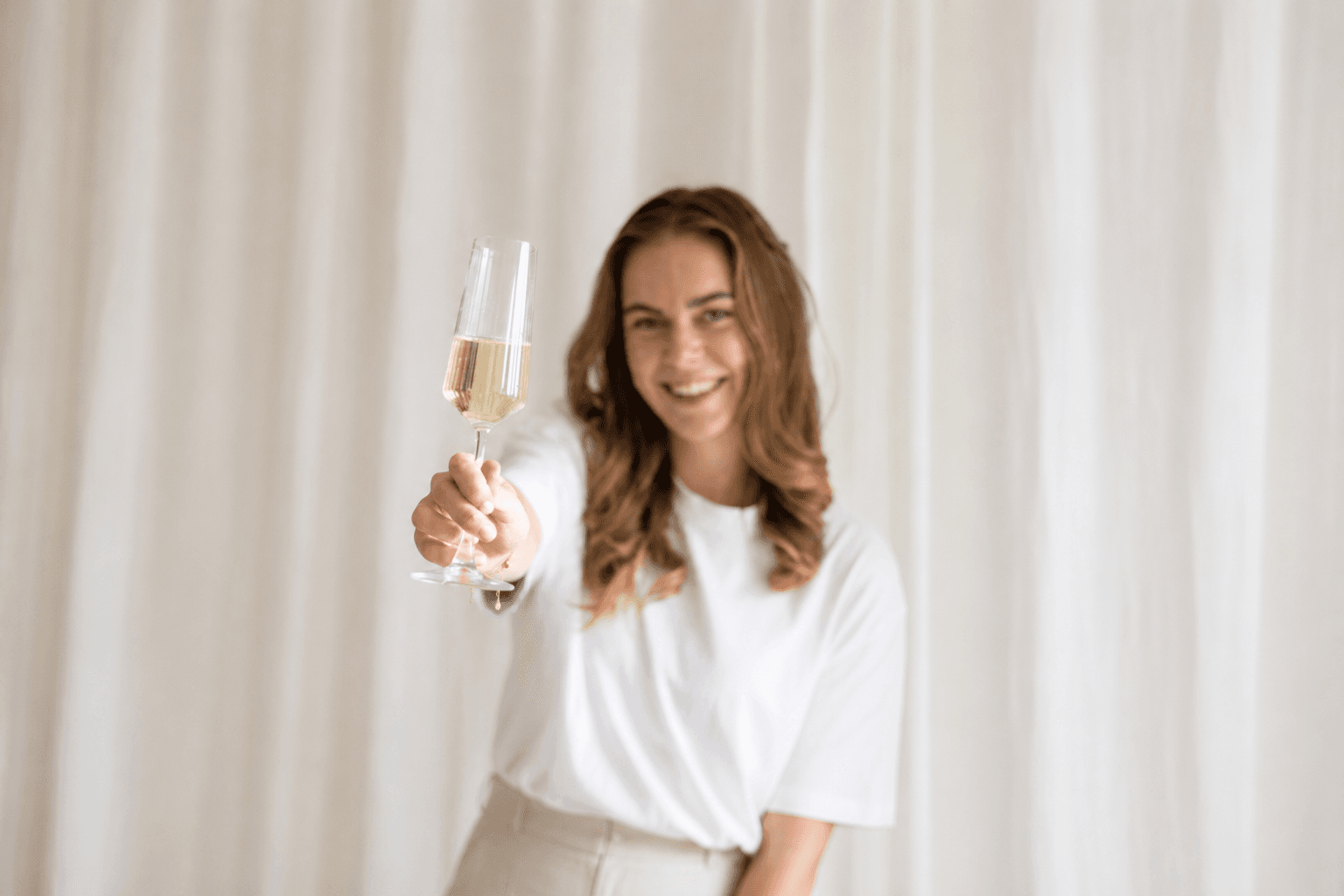 Rianda heft een glas cava voor crèmekleurige gordijnen