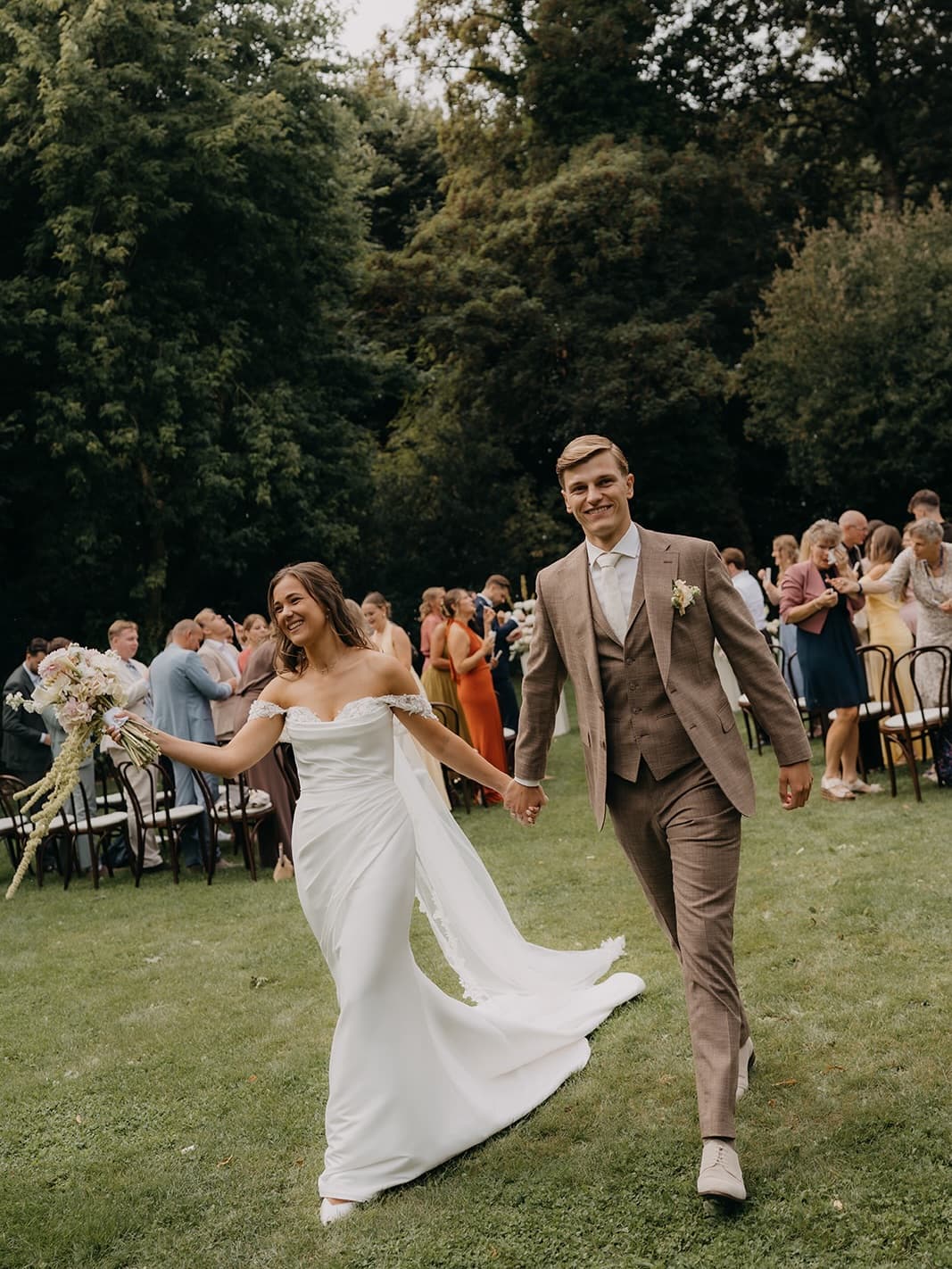Manon en Nick lopen hand in hand tussen hun gasten bij de buitenceremonie