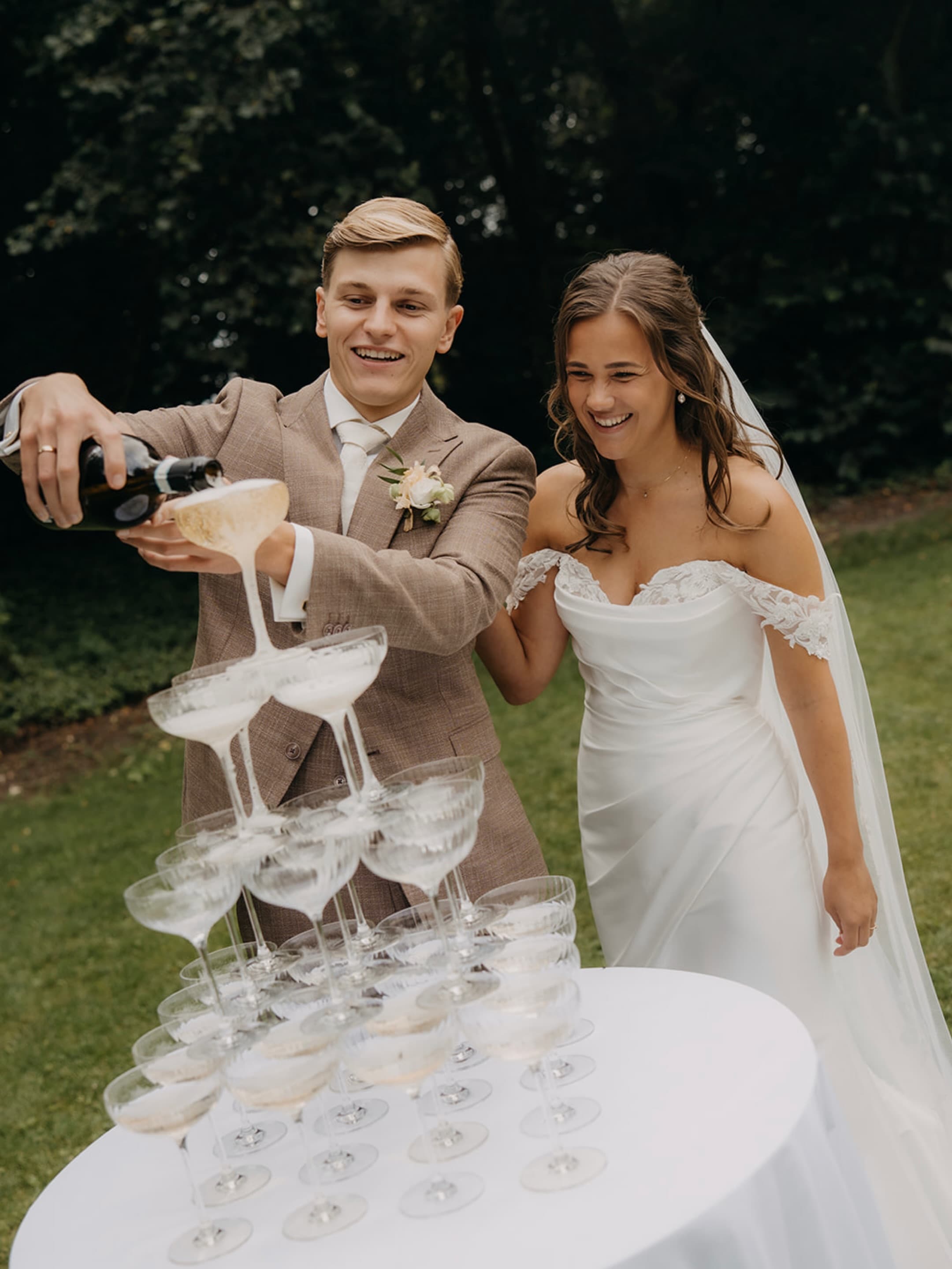 Manon en Nick schenken samen champagne in een toren van glazen op een witte tafel